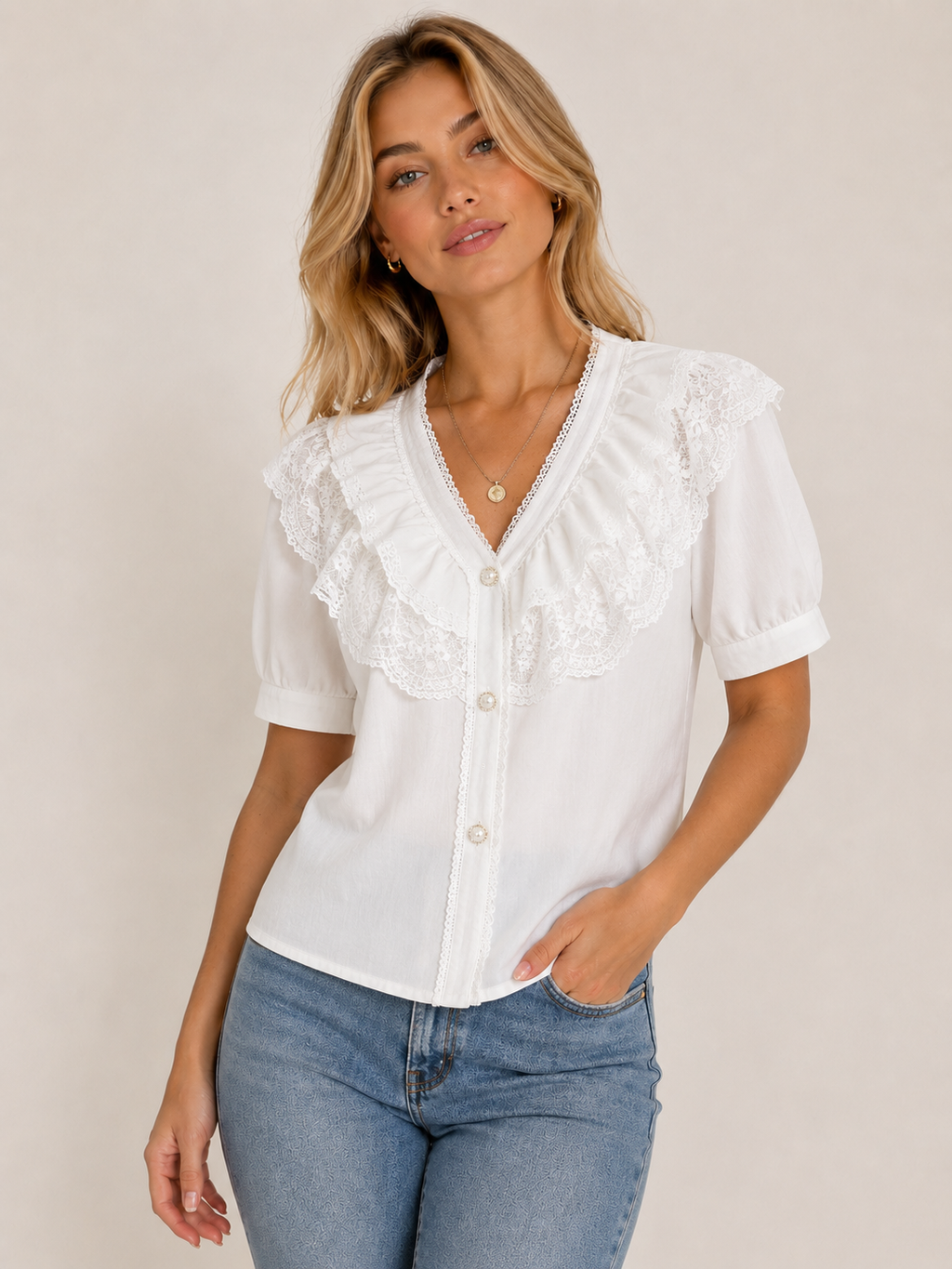 A woman wearing a white short-sleeve blouse with ruffled lace trim and button-front detailing, paired with blue jeans, against a plain beige studio background.