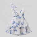 White sleeveless ruffled dress with blue floral print, thin crisscross straps, and a lace-up front, shown on a light gray background.