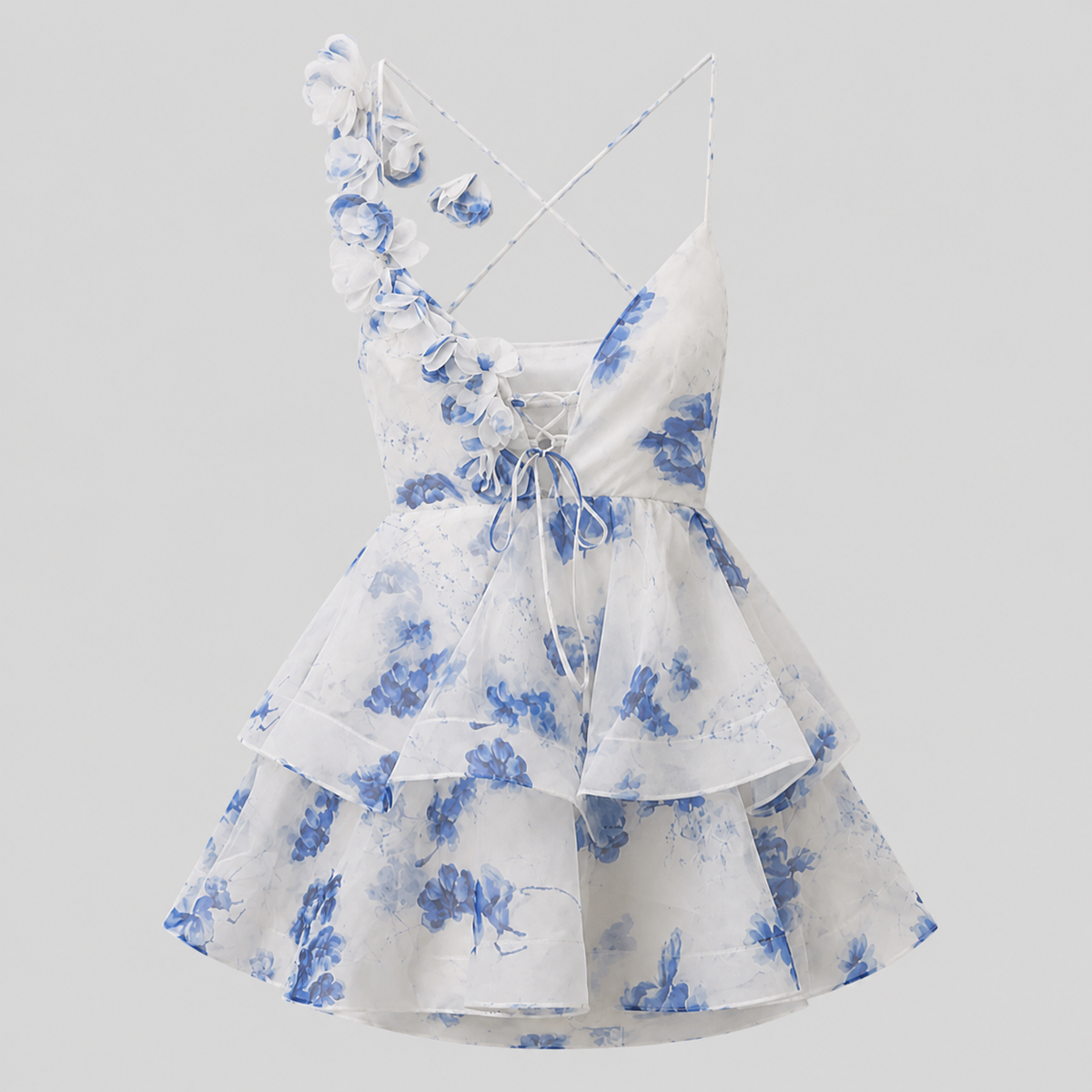 White sleeveless ruffled dress with blue floral print, thin crisscross straps, and a lace-up front, shown on a light gray background.