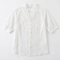 A white short-sleeve blouse with intricate floral eyelet embroidery and a button-down front, displayed flat against a white background.