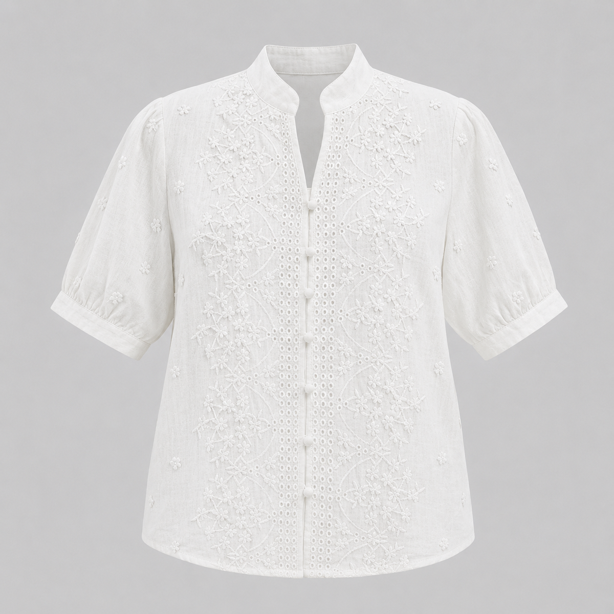 White short-sleeve eyelet blouse with a mandarin collar and button front, shown on a neutral gray background.