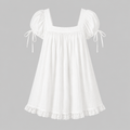 A white cotton dress with puff sleeves, tie details on the sleeves, a square neckline, and a ruffled lace hem, shown against a solid gray background.