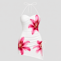 White halter mini dress with a sweetheart neckline, ruched bodice, and pink lily floral print, shown on a light gray background.