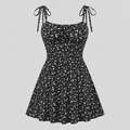 A black sleeveless fit-and-flare dress with a white daisy floral print, tie-shoulder straps, and a sweetheart neckline, shown against a solid light gray background.