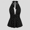 A black halter-neck dress with white polka dots, featuring a tie-front neckline, a gathered waist, and a flared skirt, shown against a solid light gray background.