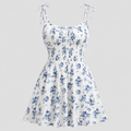 White sleeveless skater dress with a blue floral print, featuring thin adjustable tie straps and a gathered empire waist, shown against a solid light gray background.
