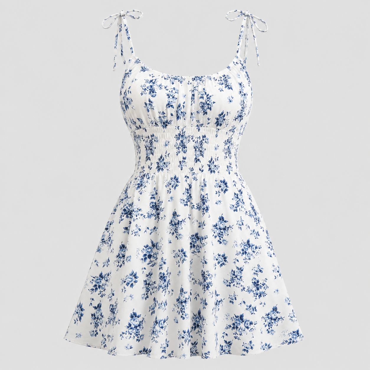 White sleeveless skater dress with a blue floral print, featuring thin adjustable tie straps and a gathered empire waist, shown against a solid light gray background.