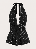 A black halter-neck dress with a white polka dot pattern, featuring a tie-neck design and a flared skirt, shown against a light beige background.